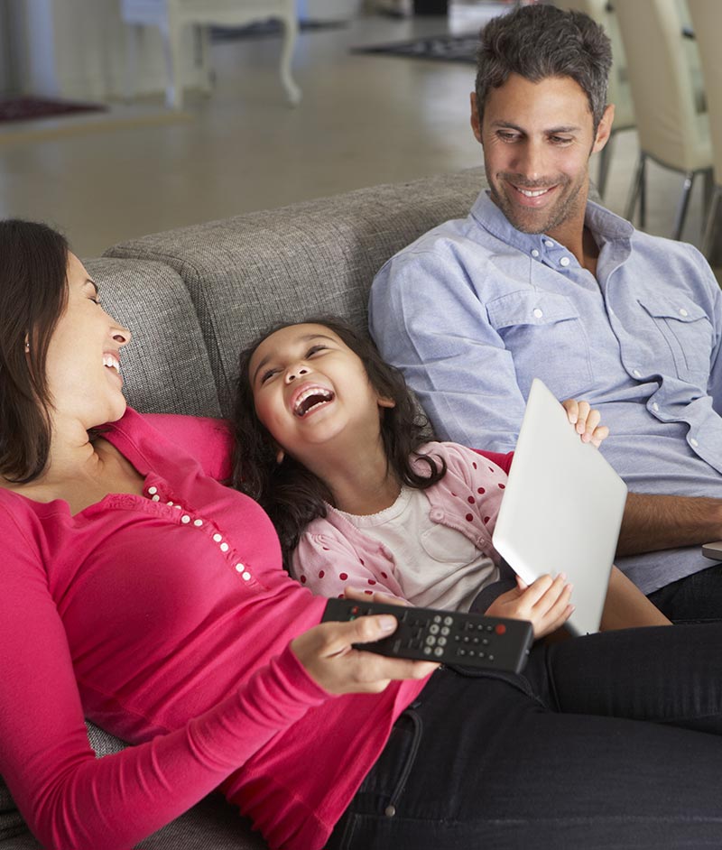 Laughing family on couch holding TV remote and tablet