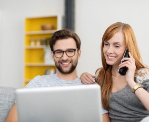 Young, attractive couple using home phone and laptop